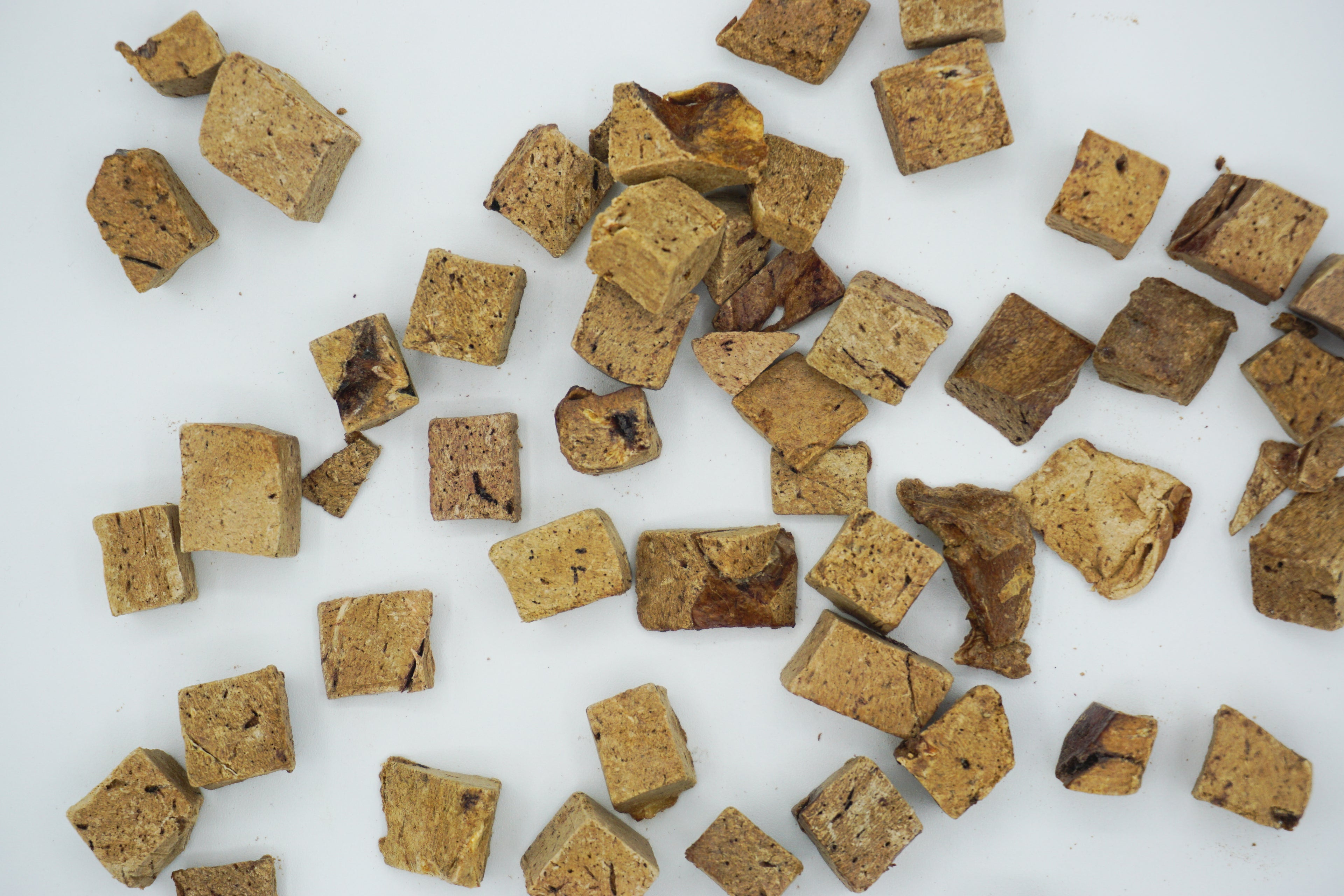 Freeze-dried bison liver treats spread out on a white surface