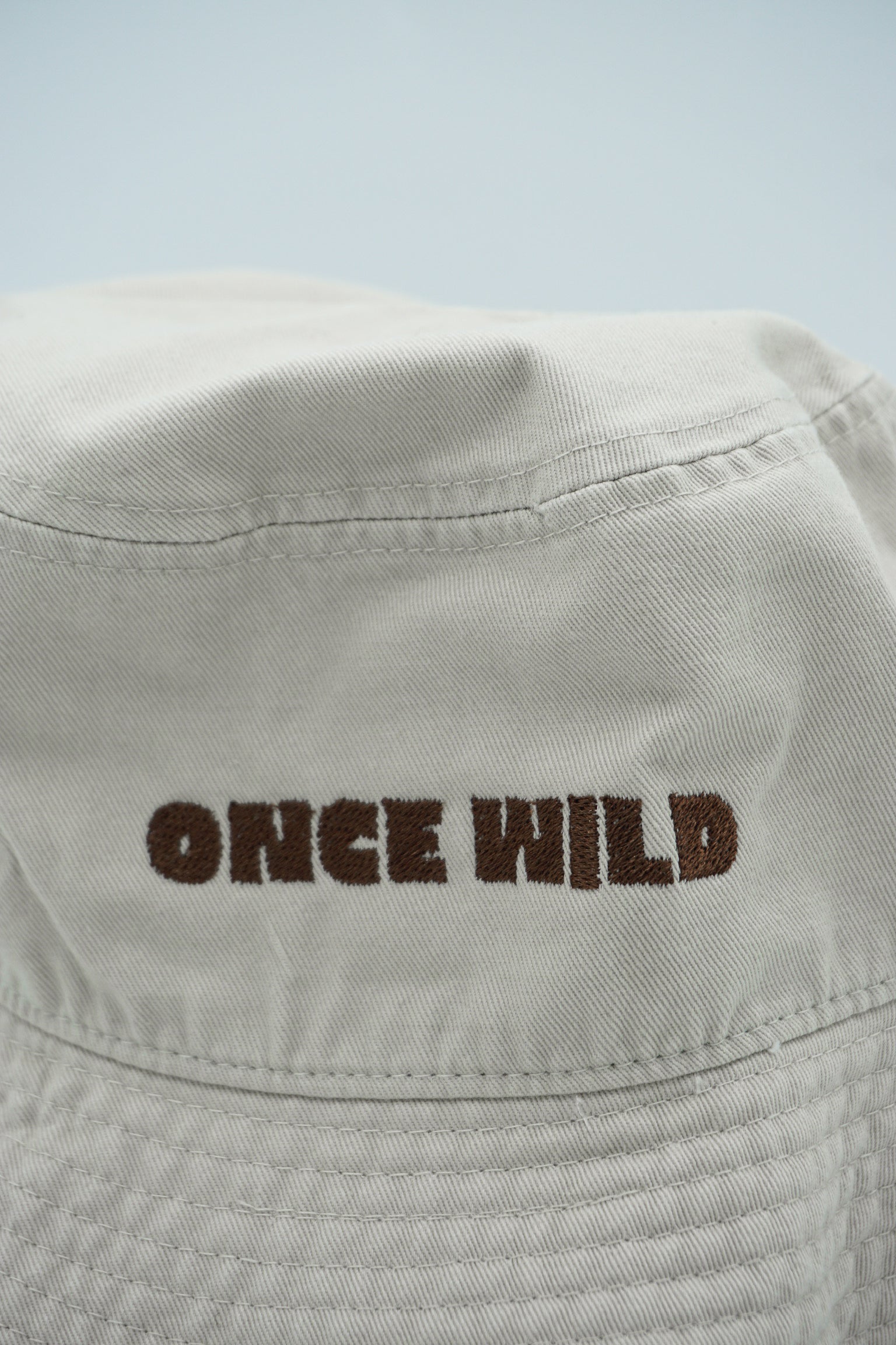 Beige bucket hat with 'Once Wild' text on a light gray background