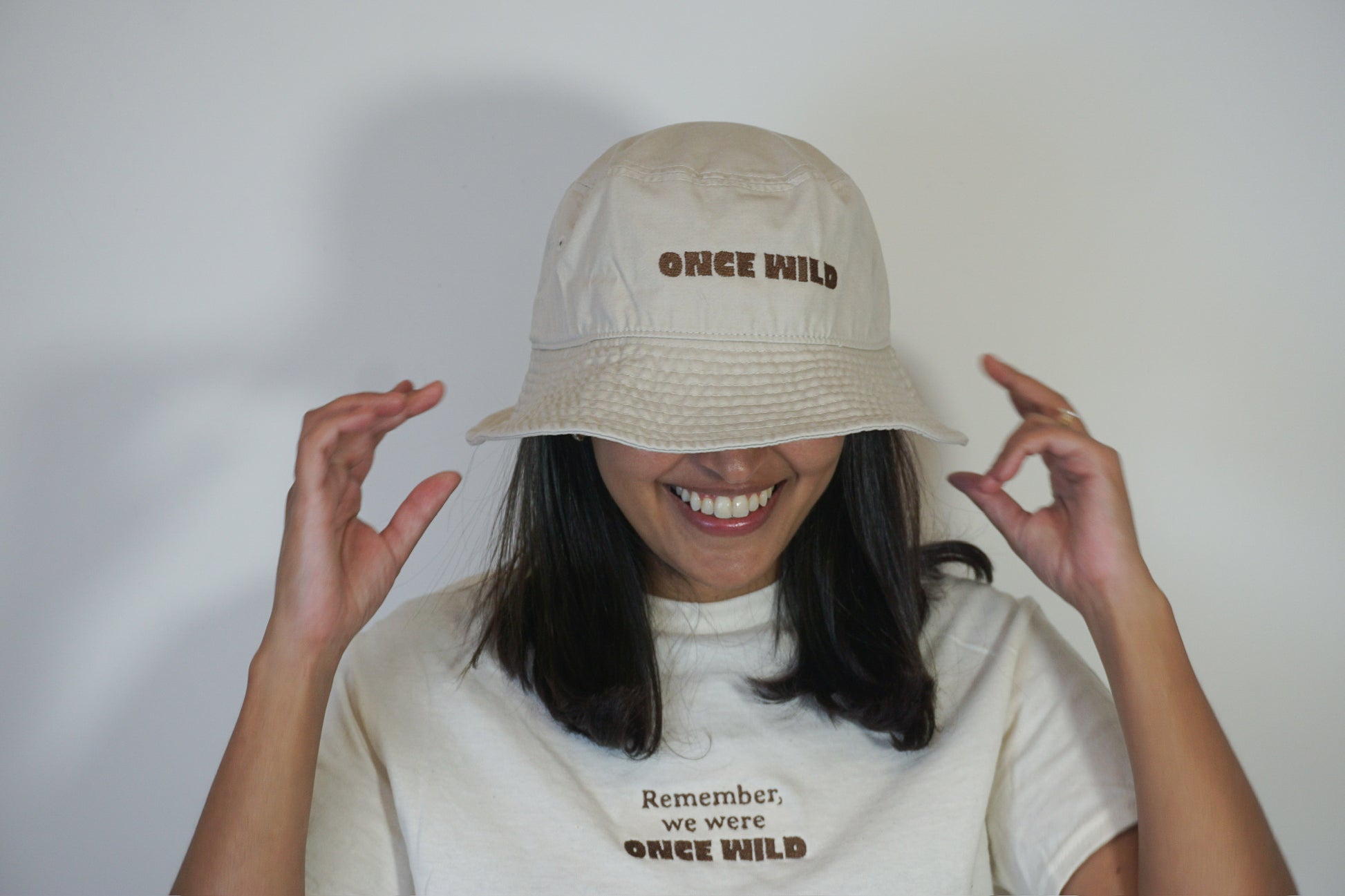 Person wearing a beige bucket hat with 'Once Wild' text, smiling against a plain background
