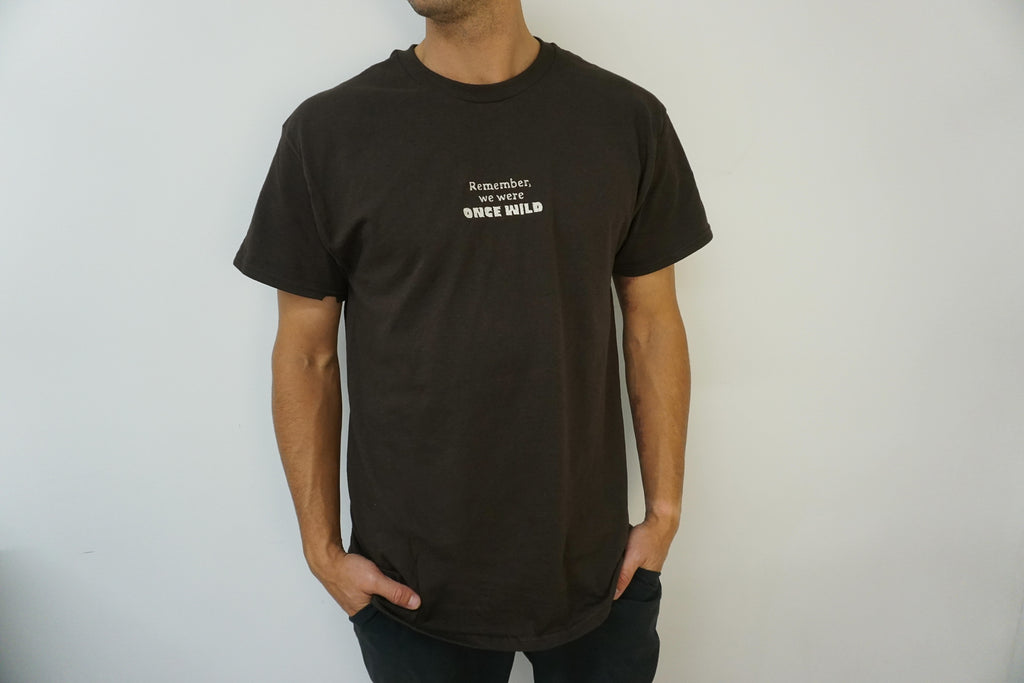 Man wearing a brown t-shirt with text on a plain background that says "Remember, we were Once Wild" 