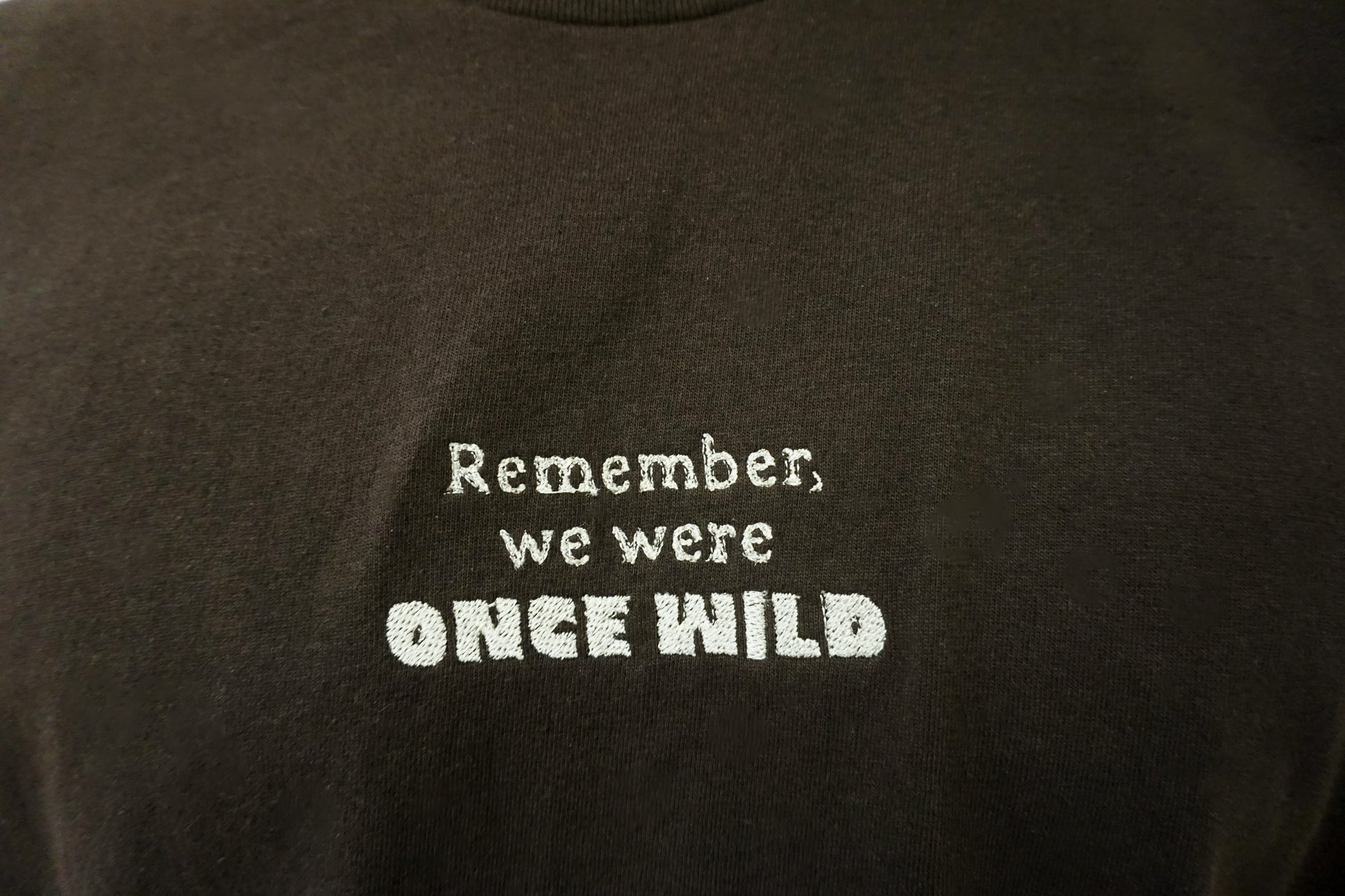 Brown T-shirt with white embroidered text that says "Remember, we were Once Wild"
