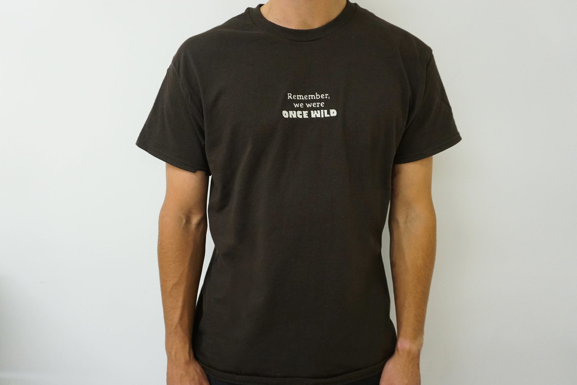 Man wearing a brown t-shirt with white text on a plain background that says "Remember, we were Once Wild"