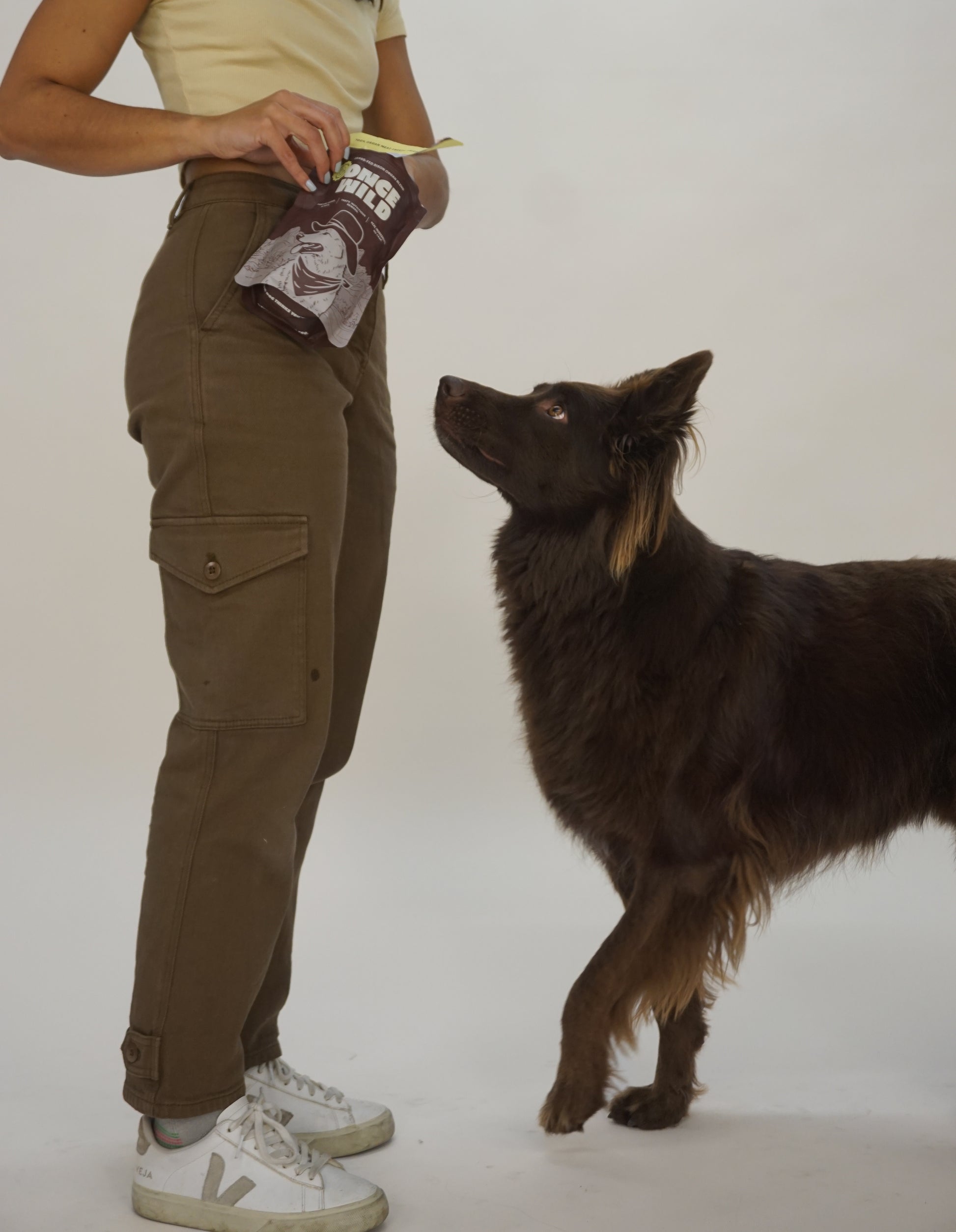 Person feeding a dog treats from a Once Wild treats pouch