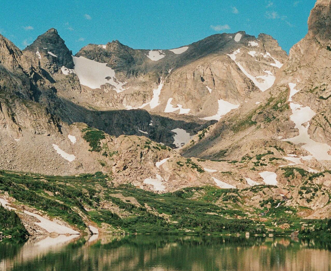 Mountain landscape with a lake reflecting the peaks under a clear blue sky.