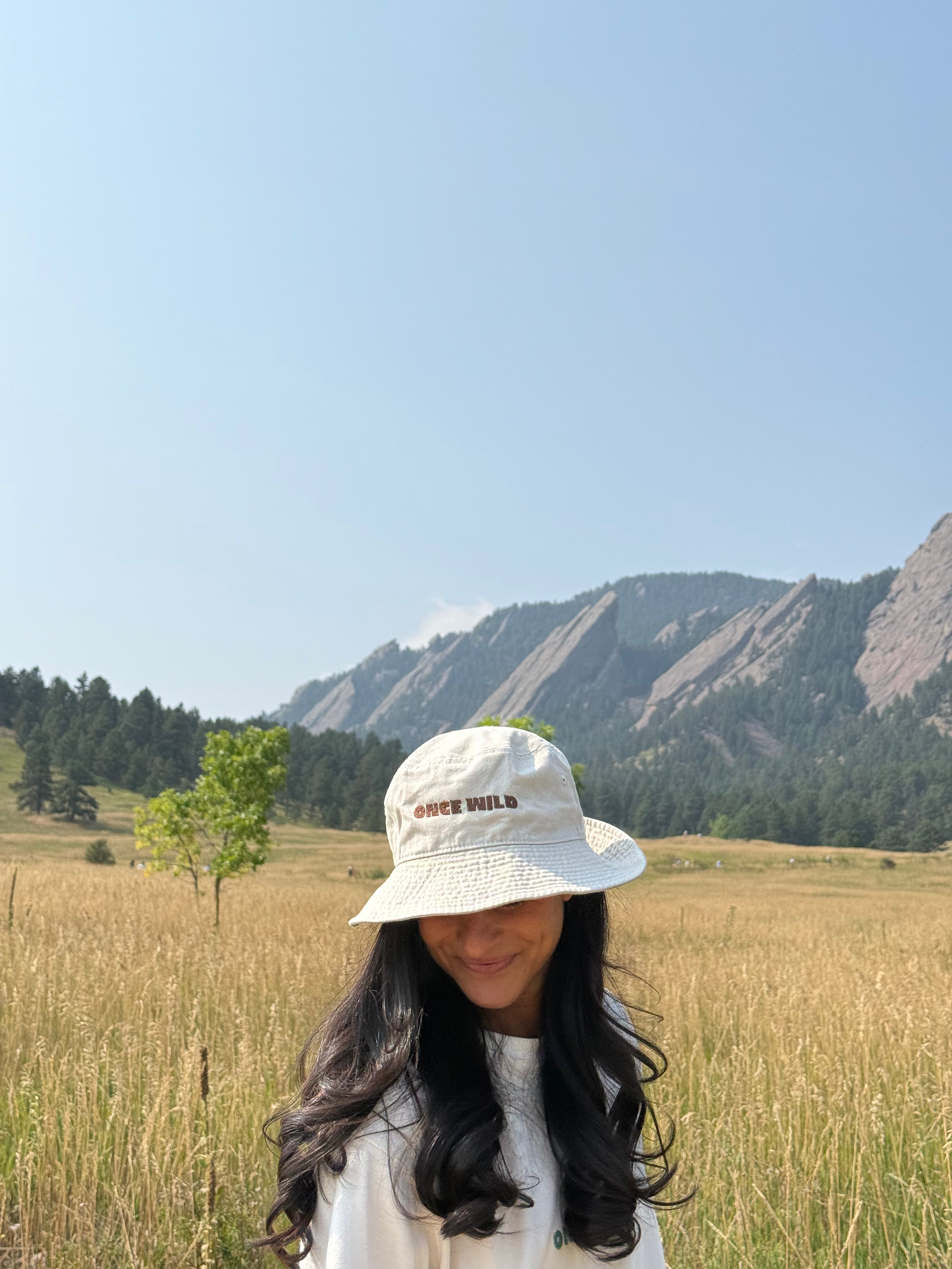 Woman wearing a white bucket hat in a field with mountains in the background