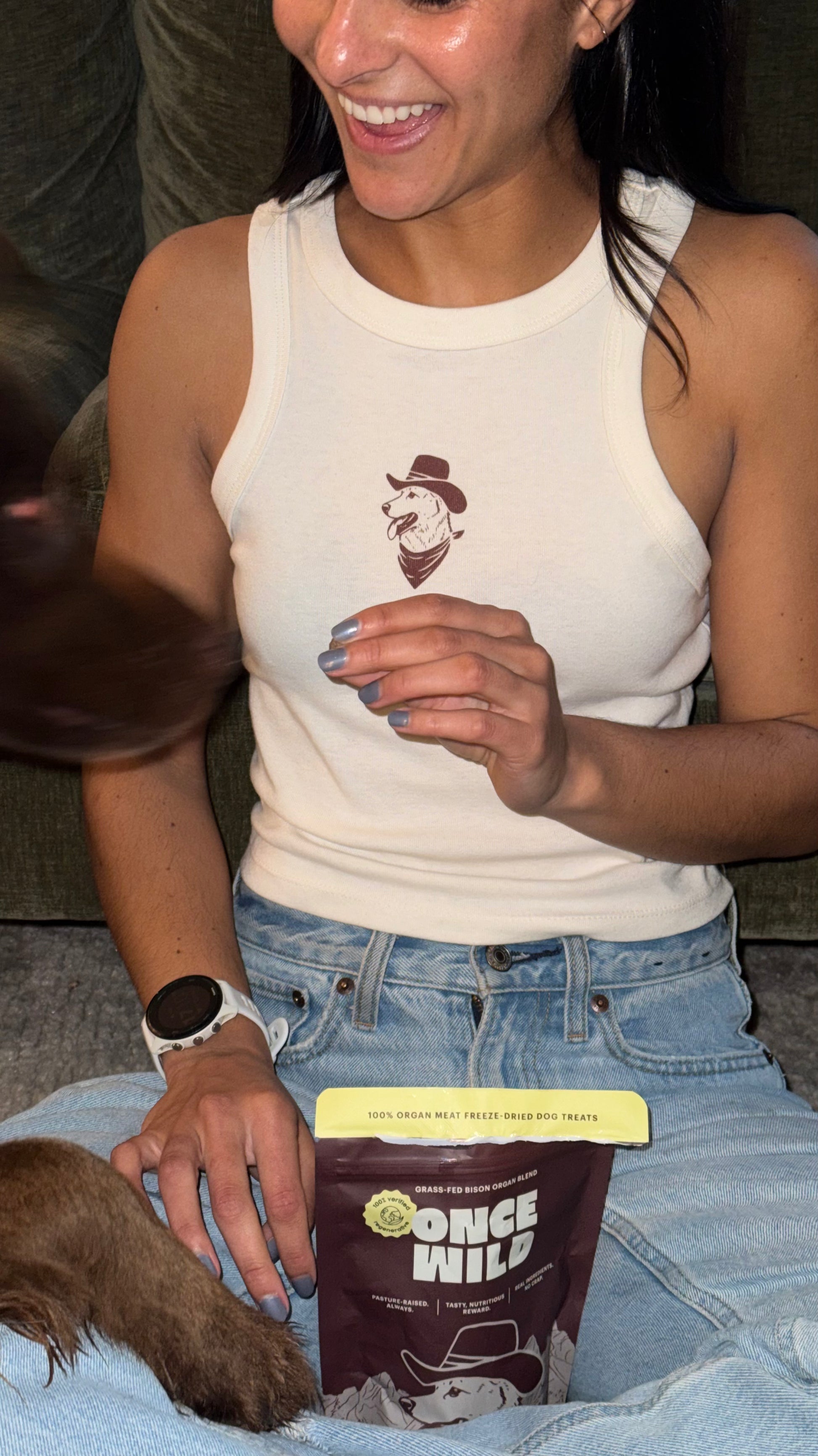Person wearing a white tank top with a logo, holding a bag of 'Once Wild' jerky.