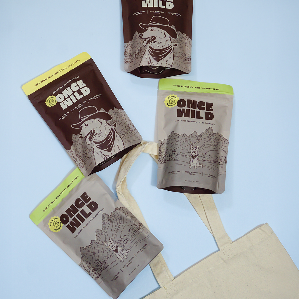 Four Once Wild dog treat packages with a tote bag gift on a light blue background