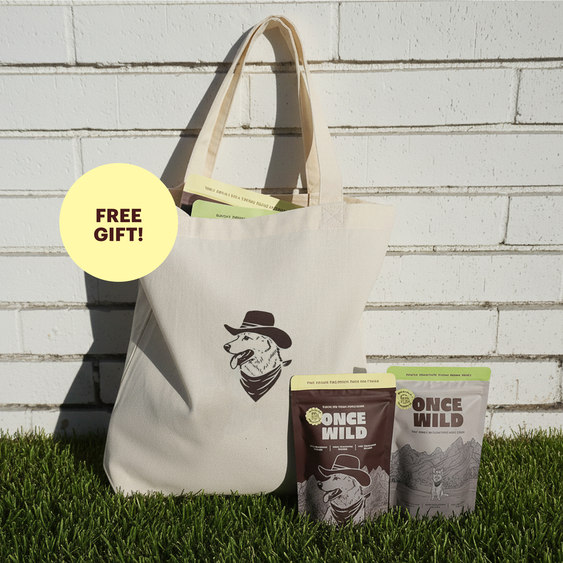Tote bag with a dog wearing a cowboy hat design and Once Wild dog treat packages grass against a white brick wall.