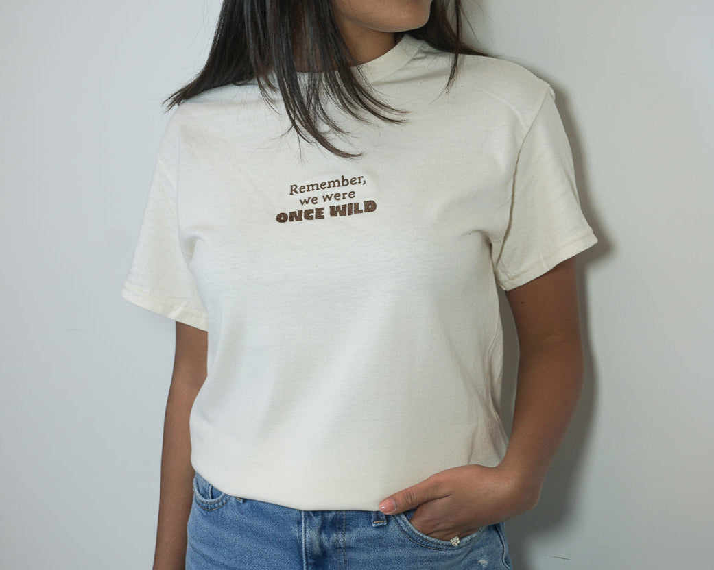 Person wearing a white t-shirt with text 'Remember, we were once wild' on a plain background